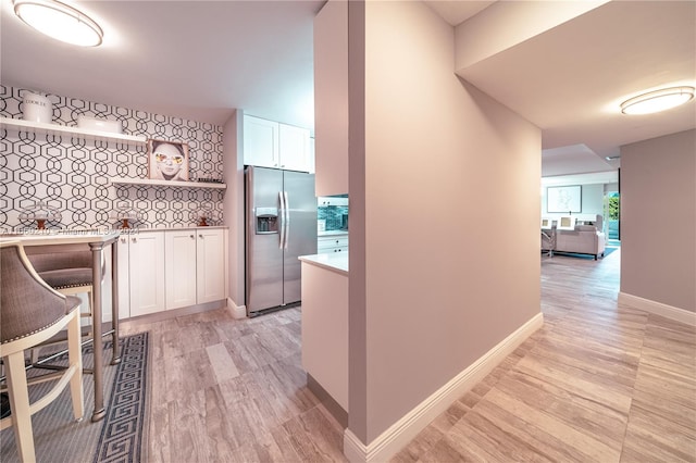 kitchen with stainless steel refrigerator with ice dispenser, light wood-type flooring, backsplash, and white cabinetry