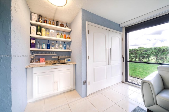 interior space featuring light stone counters, light tile patterned flooring, sink, and white cabinetry