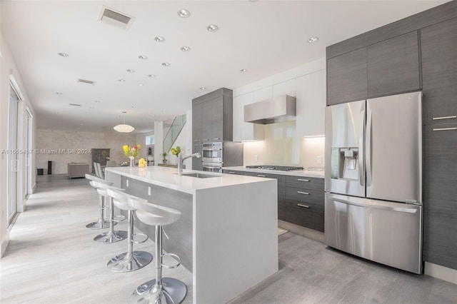 kitchen featuring sink, a kitchen breakfast bar, stainless steel appliances, a center island with sink, and exhaust hood