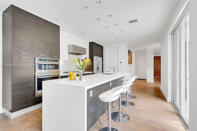 kitchen featuring light wood-type flooring, a kitchen island with sink, sink, a breakfast bar area, and appliances with stainless steel finishes