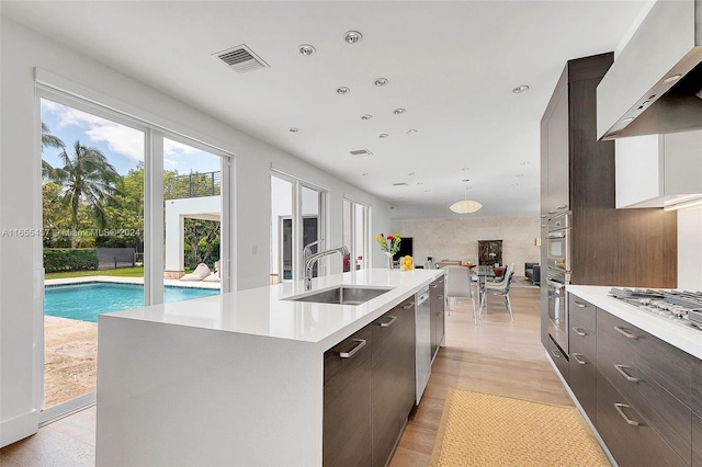 kitchen featuring light countertops, wall chimney range hood, a sink, and modern cabinets