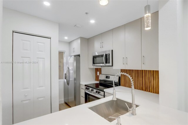 kitchen with kitchen peninsula, pendant lighting, stainless steel appliances, hardwood / wood-style floors, and sink