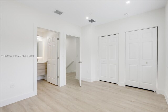 unfurnished bedroom with light hardwood / wood-style flooring, two closets, and ensuite bathroom