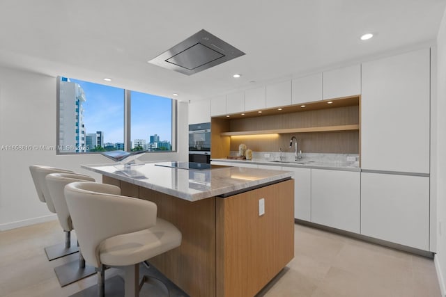 kitchen featuring white cabinetry, sink, a center island, black appliances, and light stone countertops