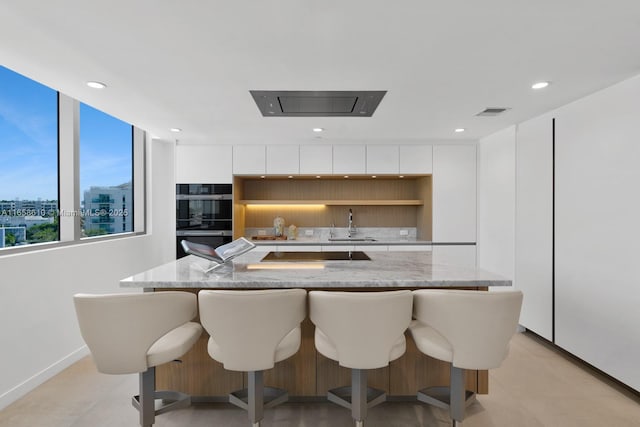 kitchen featuring light stone countertops, a kitchen island with sink, white cabinets, and black appliances