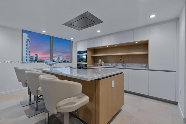 kitchen featuring sink, white cabinetry, light stone counters, a kitchen island, and black electric stovetop