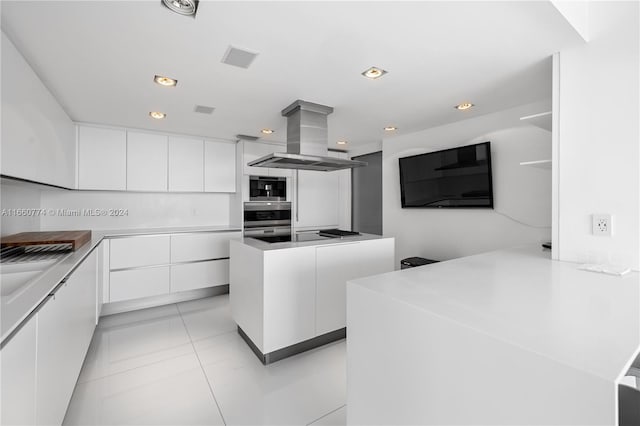 kitchen featuring light tile patterned floors, a kitchen island, island range hood, white cabinetry, and stainless steel microwave