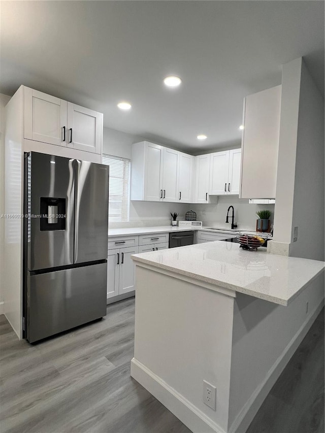 kitchen with kitchen peninsula, stainless steel fridge, light wood-type flooring, white cabinets, and light stone counters