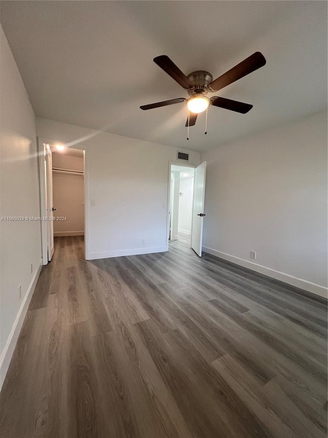 unfurnished bedroom featuring a spacious closet, a closet, dark hardwood / wood-style flooring, and ceiling fan