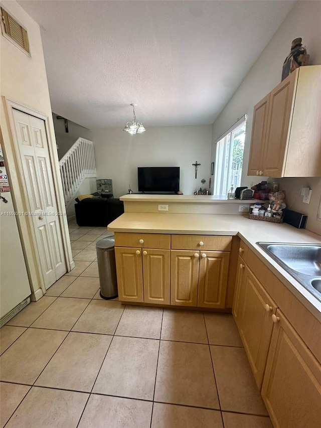 kitchen with a textured ceiling, light brown cabinets, light tile patterned floors, and decorative light fixtures