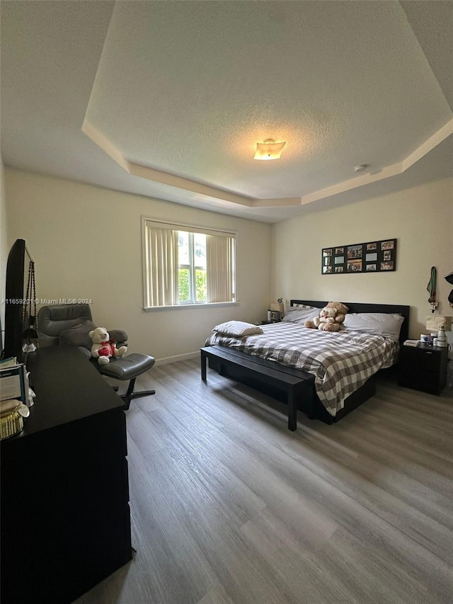 bedroom with hardwood / wood-style flooring, a tray ceiling, and a textured ceiling