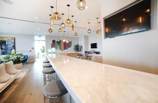 kitchen with light stone countertops, wood-type flooring, a breakfast bar area, and decorative light fixtures