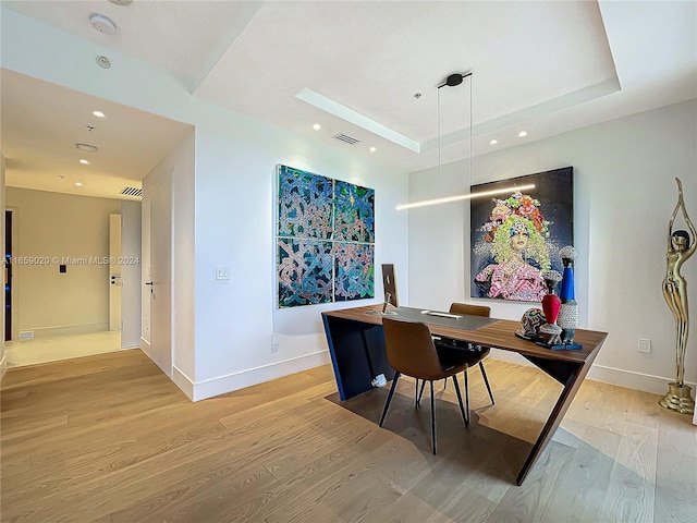 office area with a tray ceiling and light hardwood / wood-style floors