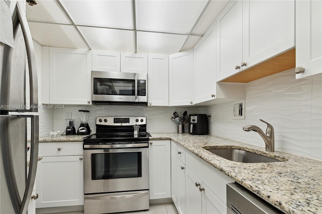 kitchen with appliances with stainless steel finishes, light stone countertops, sink, and white cabinets