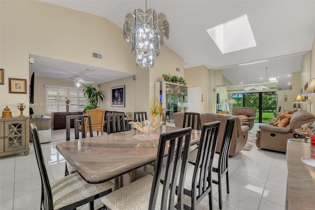 dining room featuring ceiling fan with notable chandelier, light tile patterned floors, a skylight, and high vaulted ceiling