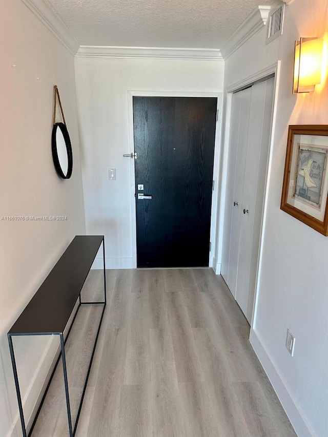 hallway featuring ornamental molding, light wood-type flooring, and a textured ceiling