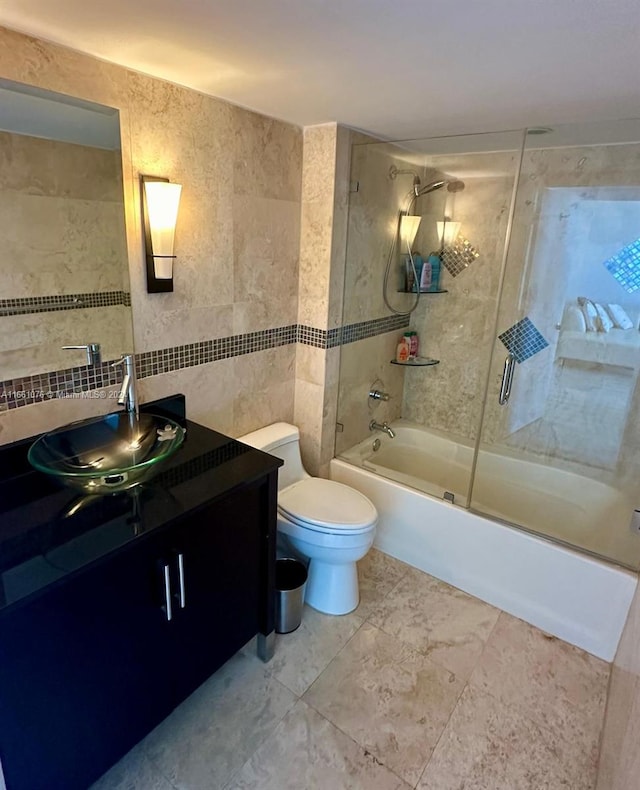 full bathroom featuring tile walls, bath / shower combo with glass door, vanity, and toilet