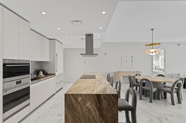 kitchen with a center island, a notable chandelier, white cabinetry, island range hood, and decorative light fixtures