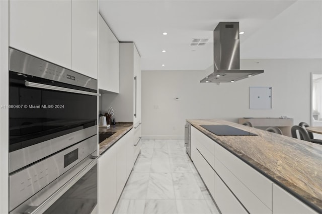 kitchen with electric panel, white cabinets, island range hood, dark stone countertops, and double oven