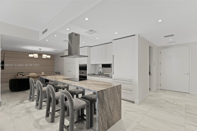 kitchen featuring light stone counters, hanging light fixtures, a kitchen island, white cabinetry, and ventilation hood