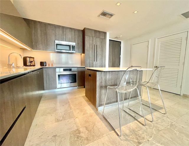 kitchen featuring a kitchen island, stainless steel appliances, a kitchen bar, dark brown cabinets, and sink