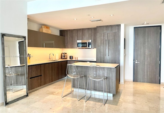 kitchen with a kitchen breakfast bar, a kitchen island, dark brown cabinetry, sink, and stovetop