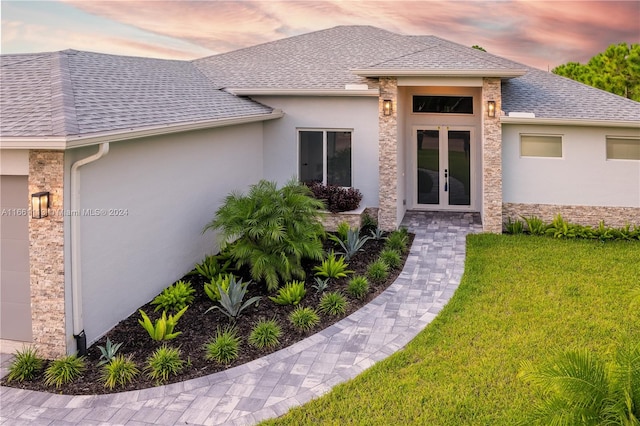 exterior entry at dusk featuring a lawn and french doors