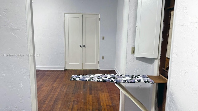 hall with baseboards, a textured wall, and dark wood-type flooring
