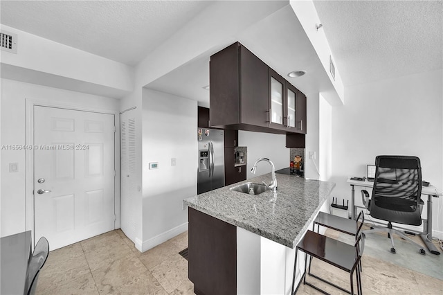 kitchen with stainless steel fridge, kitchen peninsula, a breakfast bar area, dark brown cabinets, and sink