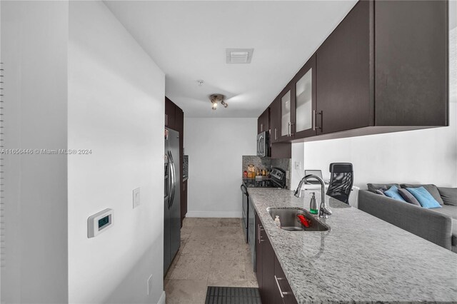 kitchen featuring dark brown cabinets, light stone counters, tasteful backsplash, sink, and stainless steel appliances