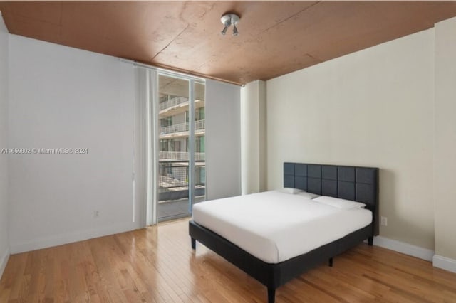 bedroom with light hardwood / wood-style floors, multiple windows, a wall of windows, and access to exterior