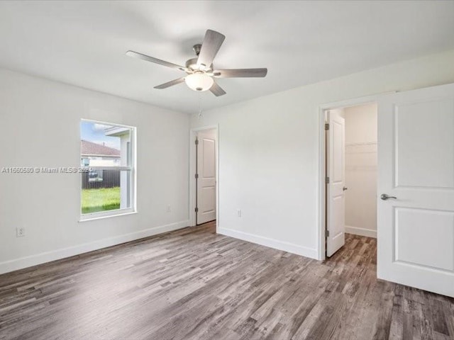 unfurnished bedroom with light wood-type flooring, ceiling fan, a walk in closet, and a closet