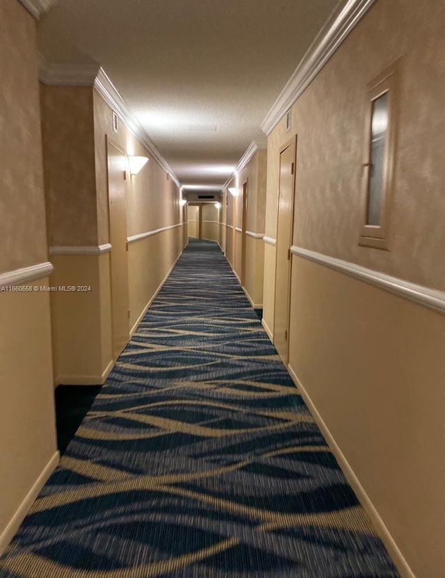 hallway with crown molding and dark colored carpet