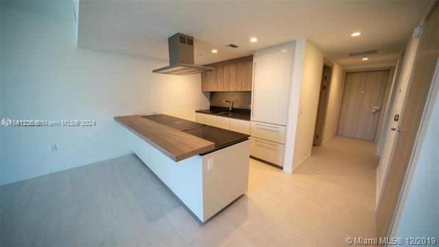 kitchen with range hood, kitchen peninsula, and sink