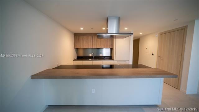 kitchen featuring wall chimney exhaust hood, kitchen peninsula, and sink