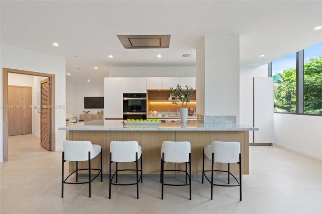 kitchen featuring a kitchen bar, sink, white cabinetry, light stone counters, and black double oven