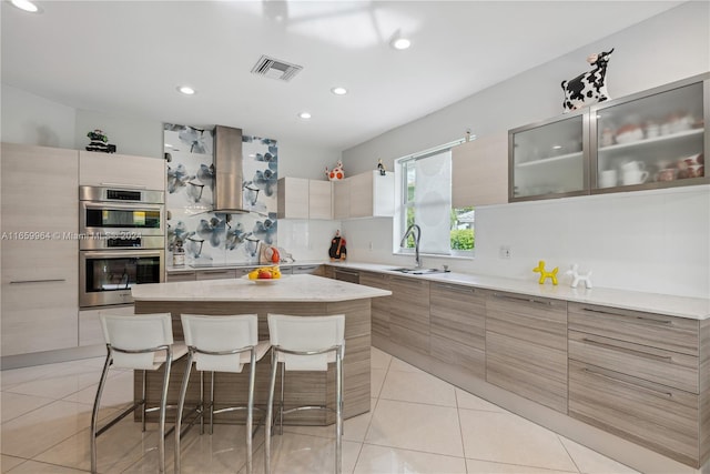 kitchen with a kitchen bar, a kitchen island, light tile patterned floors, extractor fan, and double oven