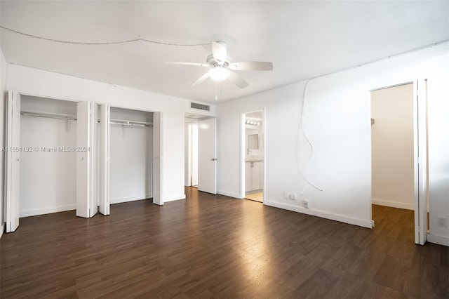 unfurnished bedroom with two closets, ceiling fan, ensuite bathroom, and dark hardwood / wood-style flooring