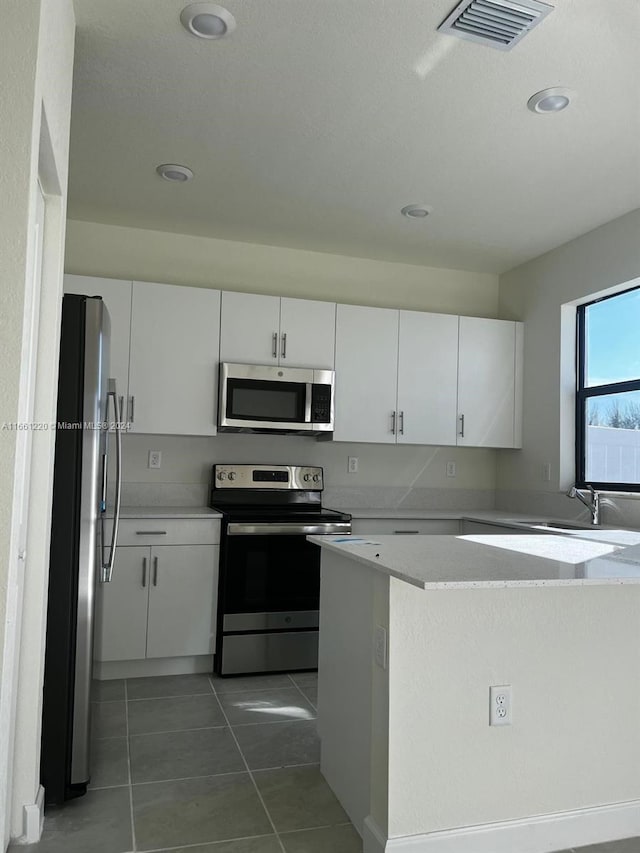 kitchen with dark tile patterned flooring, white cabinets, and stainless steel appliances