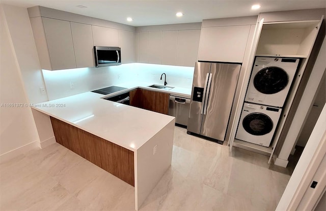 kitchen featuring sink, kitchen peninsula, stacked washer / dryer, and appliances with stainless steel finishes