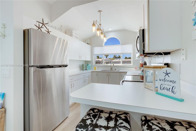 kitchen featuring white cabinets, lofted ceiling, sink, decorative light fixtures, and stainless steel appliances