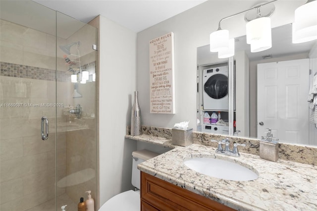 bathroom featuring vanity, stacked washing maching and dryer, a shower with shower door, and toilet