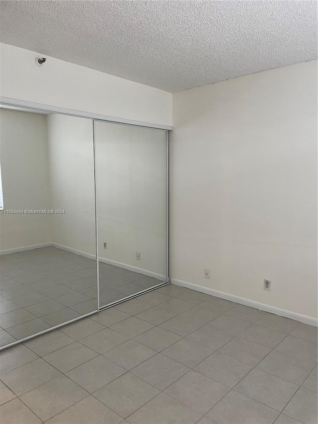 unfurnished bedroom with a closet, a textured ceiling, and light tile patterned floors