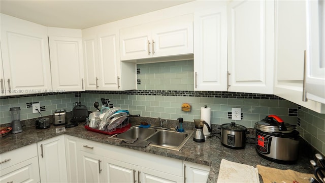 kitchen with dark stone countertops, white cabinetry, sink, and tasteful backsplash