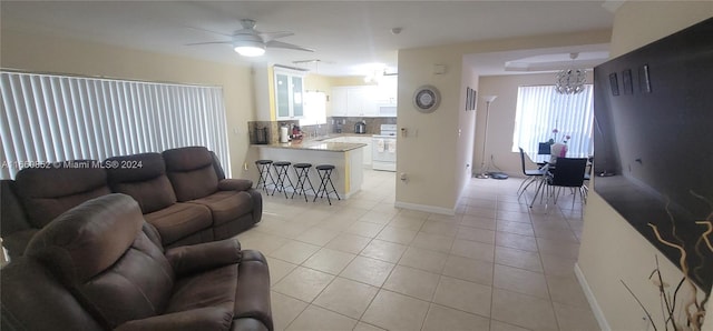 tiled living room with ceiling fan with notable chandelier