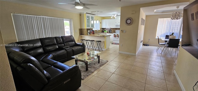 living area with baseboards, light tile patterned flooring, crown molding, and ceiling fan with notable chandelier