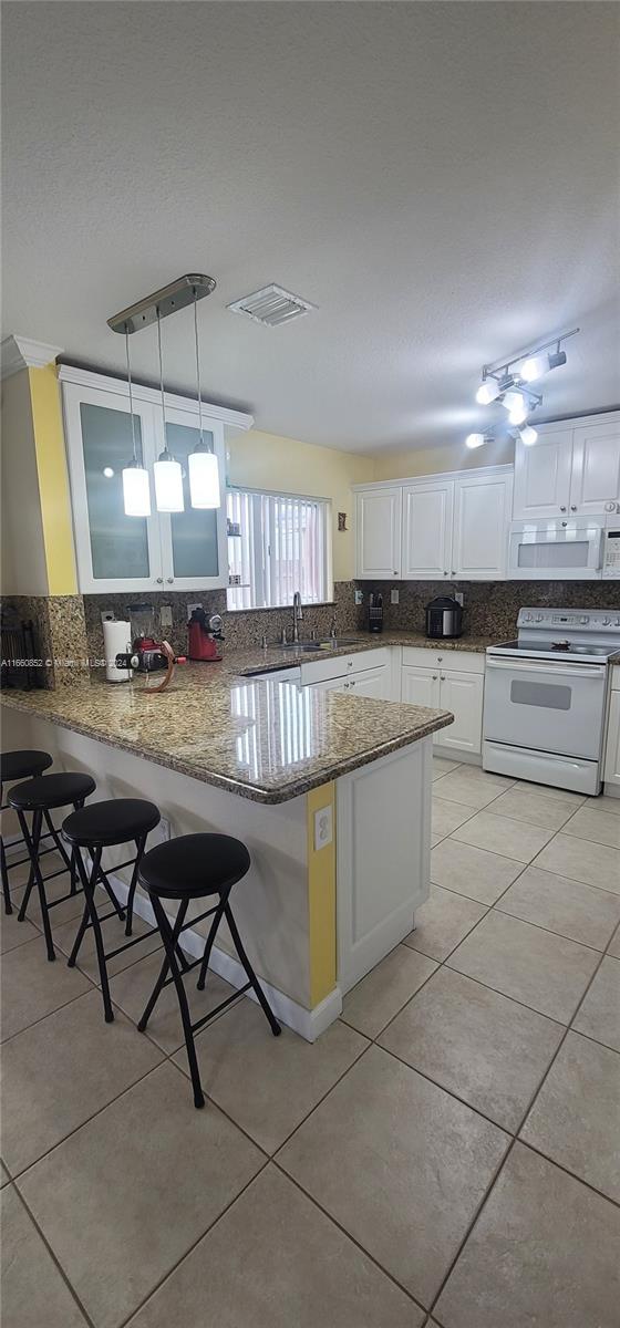 kitchen with a kitchen breakfast bar, white appliances, kitchen peninsula, and decorative light fixtures