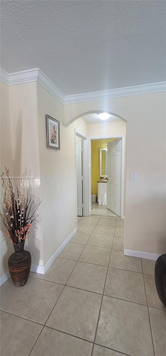 corridor featuring ornamental molding, a textured ceiling, and light tile patterned floors