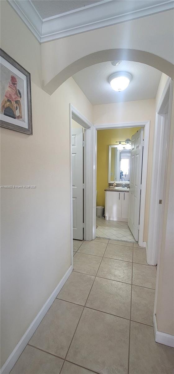 hall featuring arched walkways, light tile patterned floors, baseboards, and ornamental molding