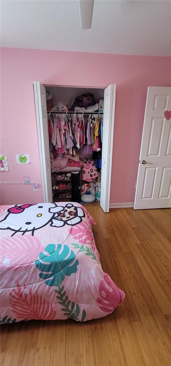 bedroom featuring ceiling fan, a closet, a textured ceiling, and wood finished floors